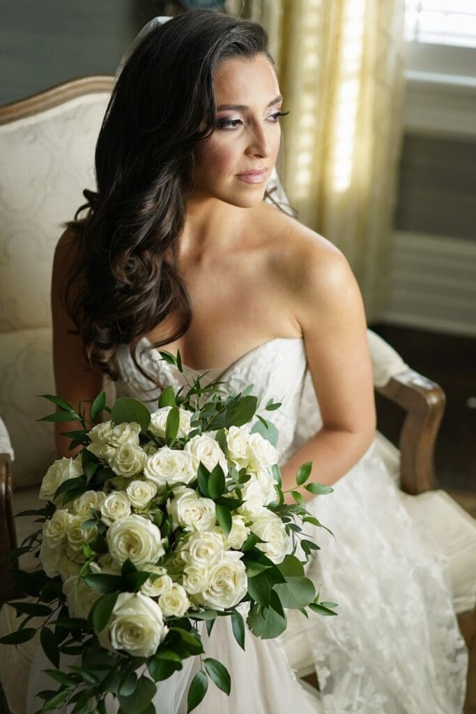 A bride holding a bouquet of white roses in a chair.