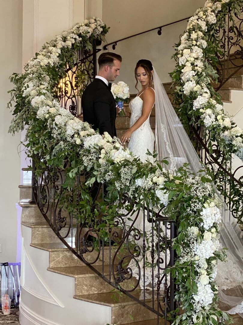 A bride and groom standing on a staircase covered in flowers.