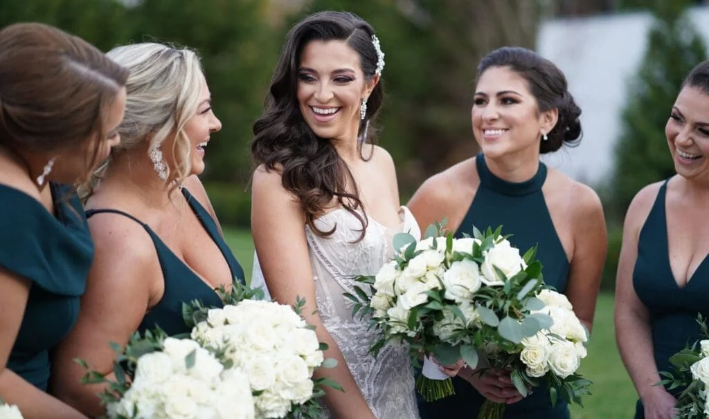 A group of bridesmaids in emerald dresses laughing.