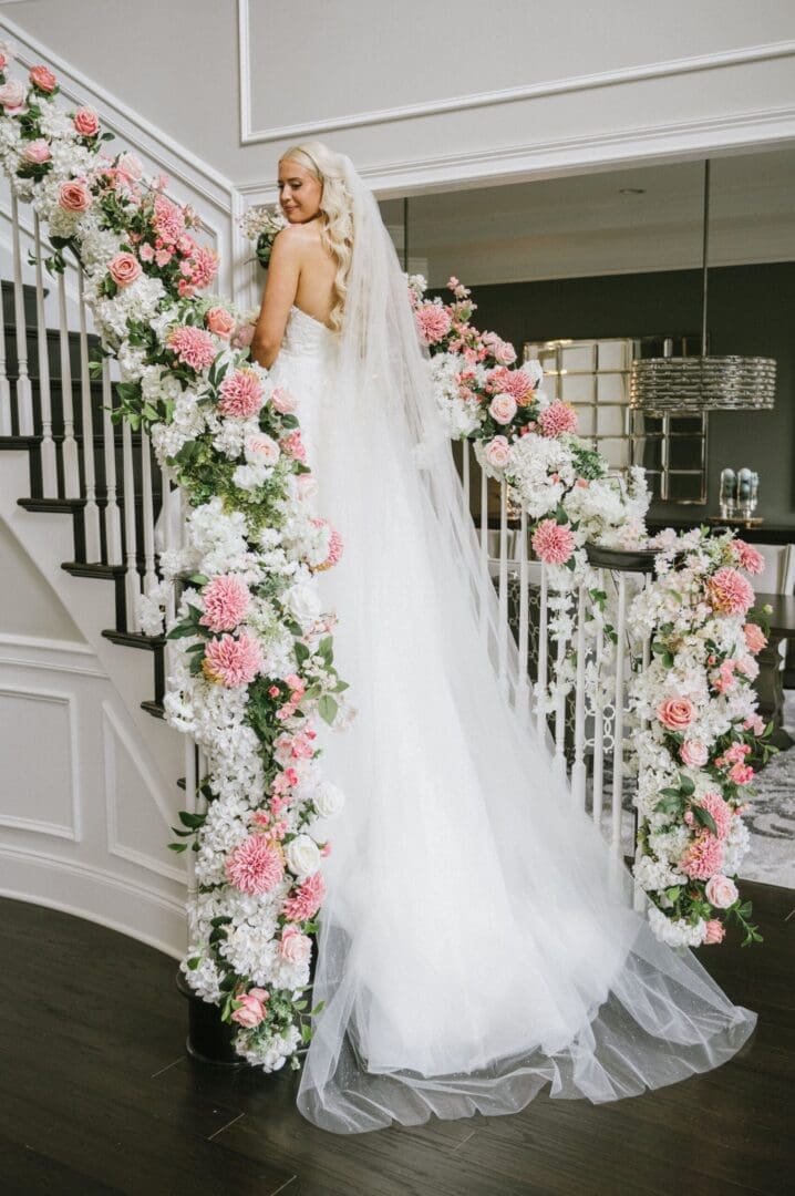 A bride in a white dress standing on a staircase decorated with flowers.
