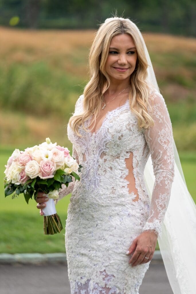 A blonde woman in a lace wedding dress holding a bouquet.