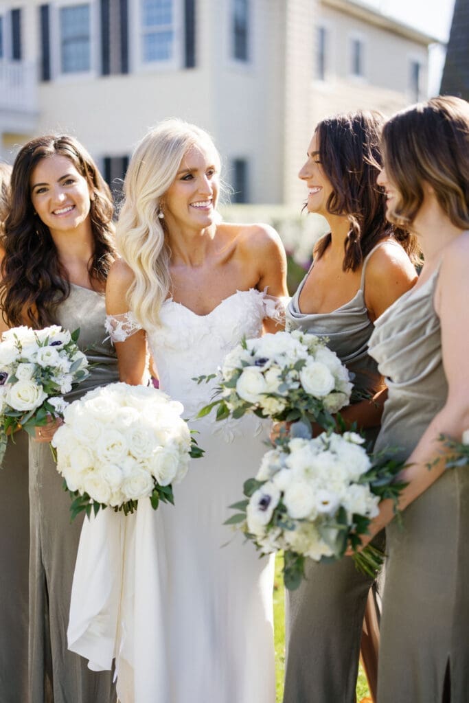 A bride and her bridesmaids are holding bouquets in front of a house.