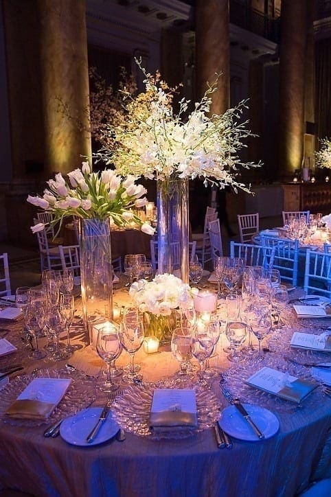 A romantic wedding tablescape adorned with white flowers and flickering candles in a spacious room.