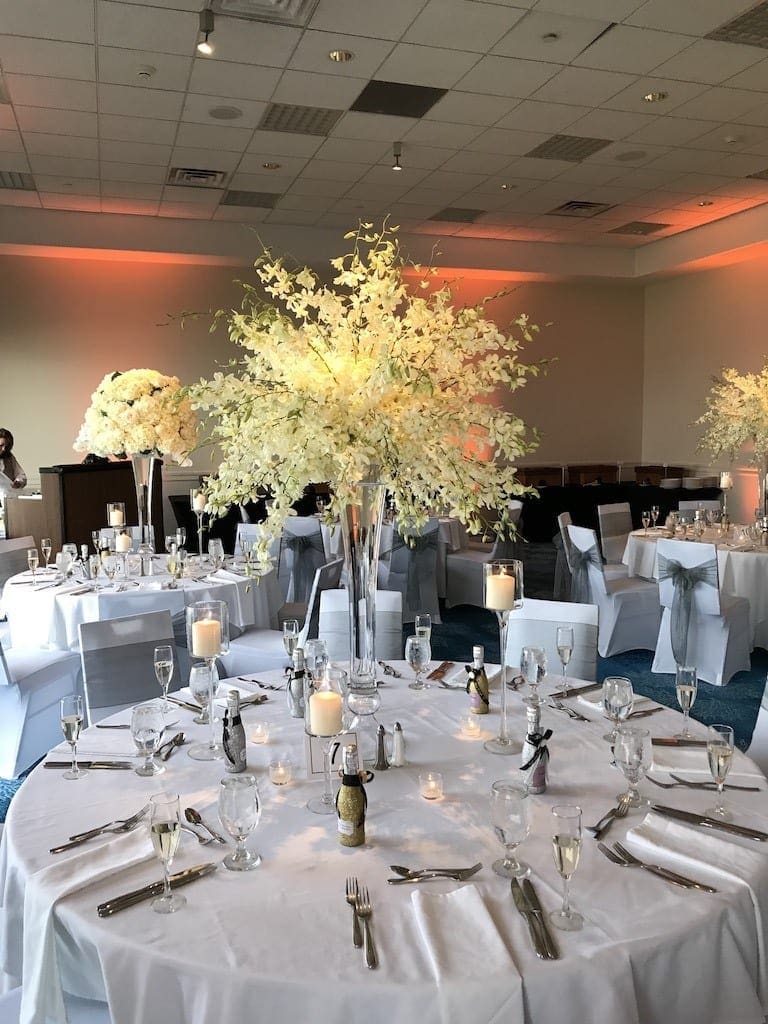 A wedding reception with a tablescape featuring white tablecloths and white flowers.
