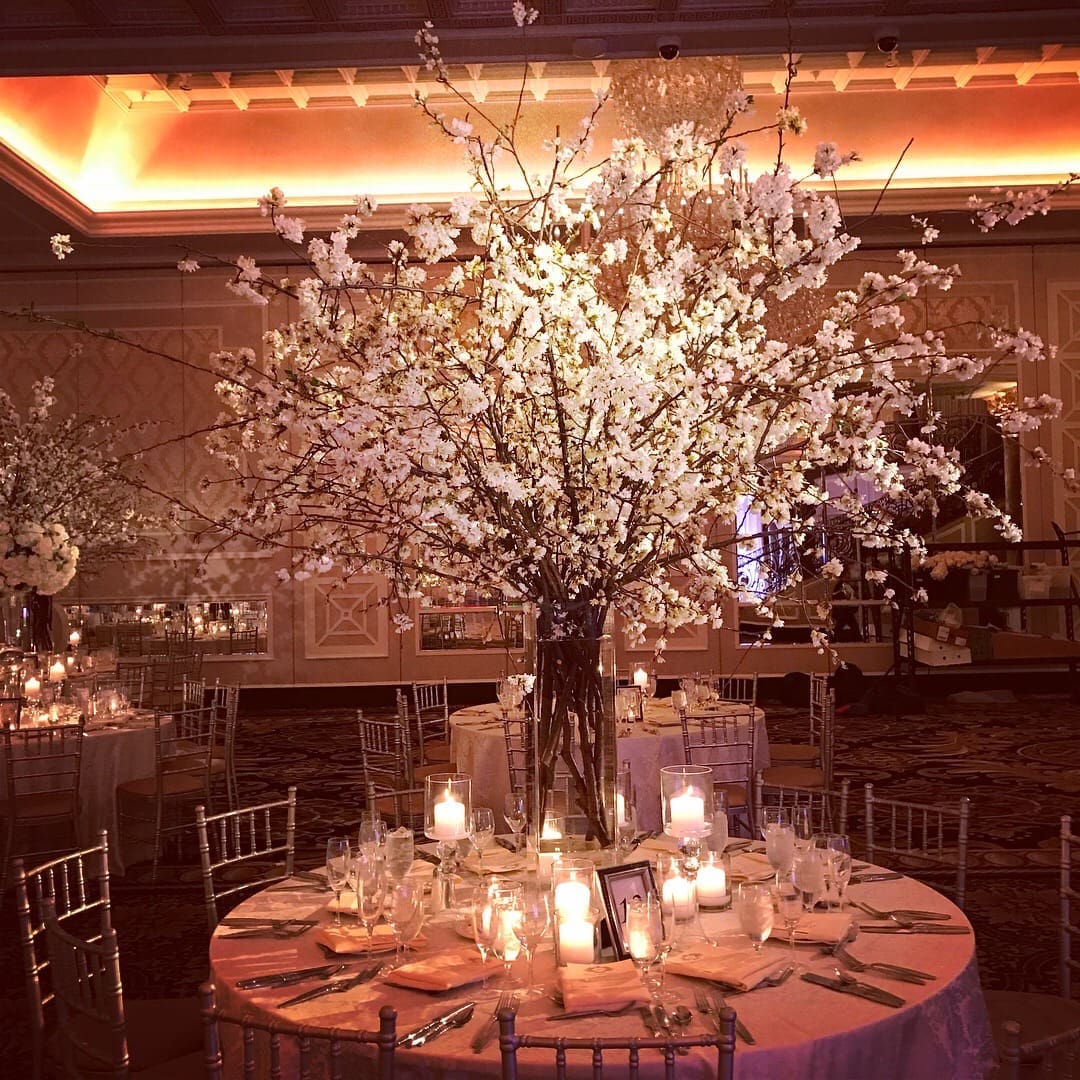 A stunning wedding tablescape adorned with white flowers and flickering candles, creating a romantic ambiance in a beautifully decorated banquet room.